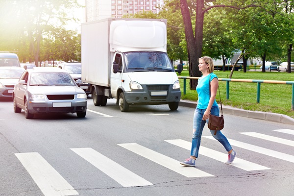 Woman walking across a crosswalk in front of cars and a delivery truck on a sunny day. (334516240)